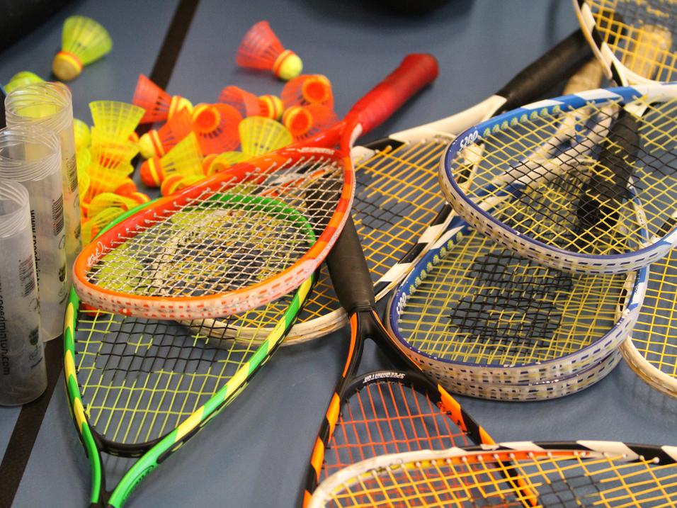 Bunte Badminton-Schläger und -Bälle liegen auf einem Tisch, umgeben von transparenten Schutzhüllen.