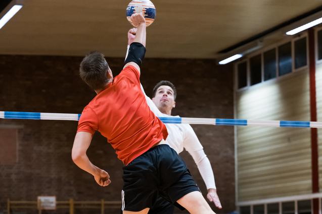 Zwei Spieler im Sprung während eines Handballspiels, einer wirft den Ball über eine Markierung.