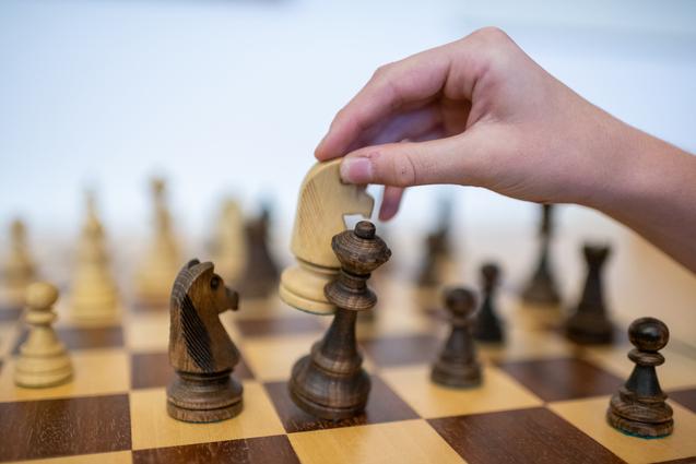 Hand bewegt einen weißen Springer auf ein Schachbrett mit braunen und weißen Figuren.