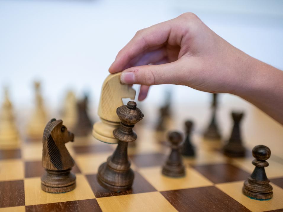 Hand bewegt einen weißen Springer auf ein Schachbrett mit braunen und weißen Figuren.