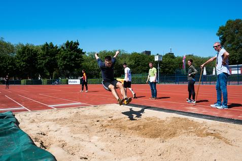 Sprinter springt vom Absprungbrett in die Sandschicht einer Weitsprunganlage, während Zuschauer am Rand stehen.