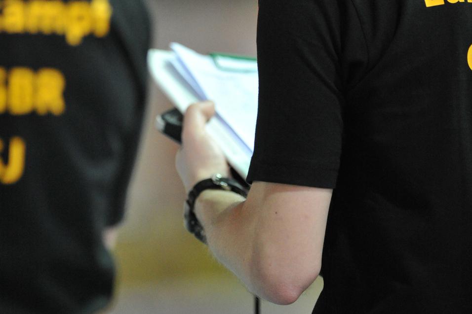Person in schwarzem T-Shirt hält ein Notizbuch und Stift, im Hintergrund leuchtende Ampeln.