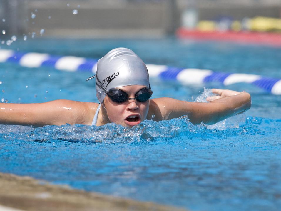 Junge Schwimmerin mit silberner Badekappe und Schwimmbrille in einem Wettkampfbecken, während sie einen Schlag ausführt.