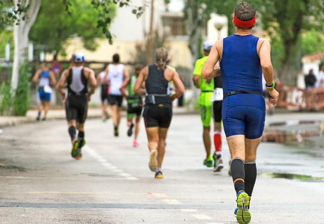 Läufer in Sportkleidung joggen auf einer Straße, umgeben von Bäumen und Gebäuden.